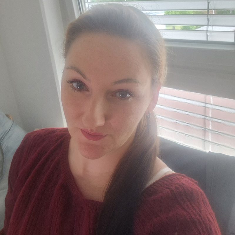 Porträt einer Frau mit braunen Haaren und rotem Pullover.