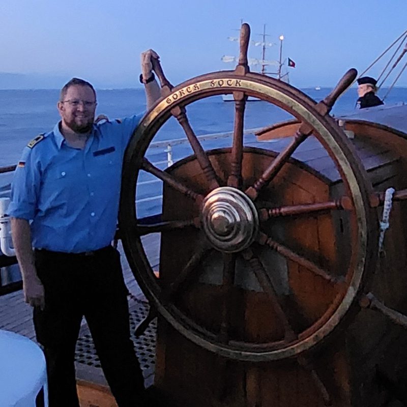 Mann in Uniform am Steuerrad eines Segelschiffs, HptBtsm Porth.
