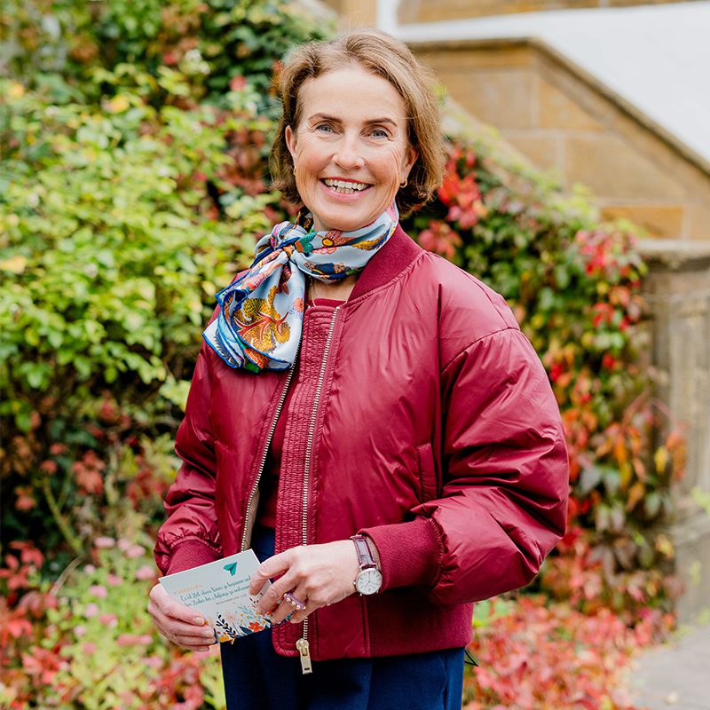Frau in roter Jacke und Schal hält Karte, lächelt. Foto 800x800px.